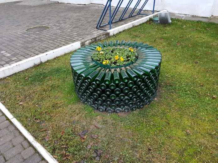 un parterre de fleurs rond avec une bordure de bouteilles en verre empilées les unes sur les autres